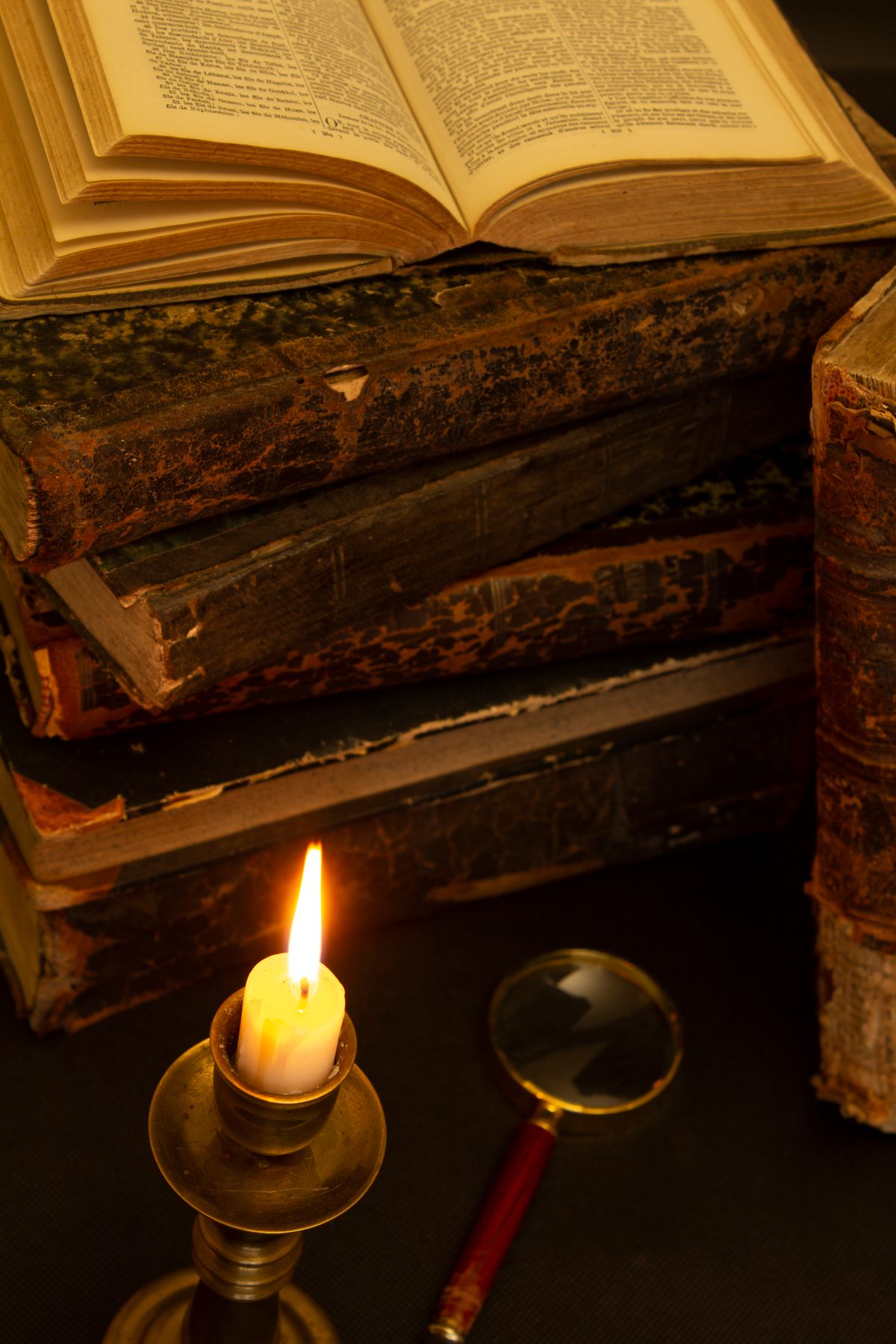 Old books, a lit candle and a magnifying glass set for an escape room puzzle