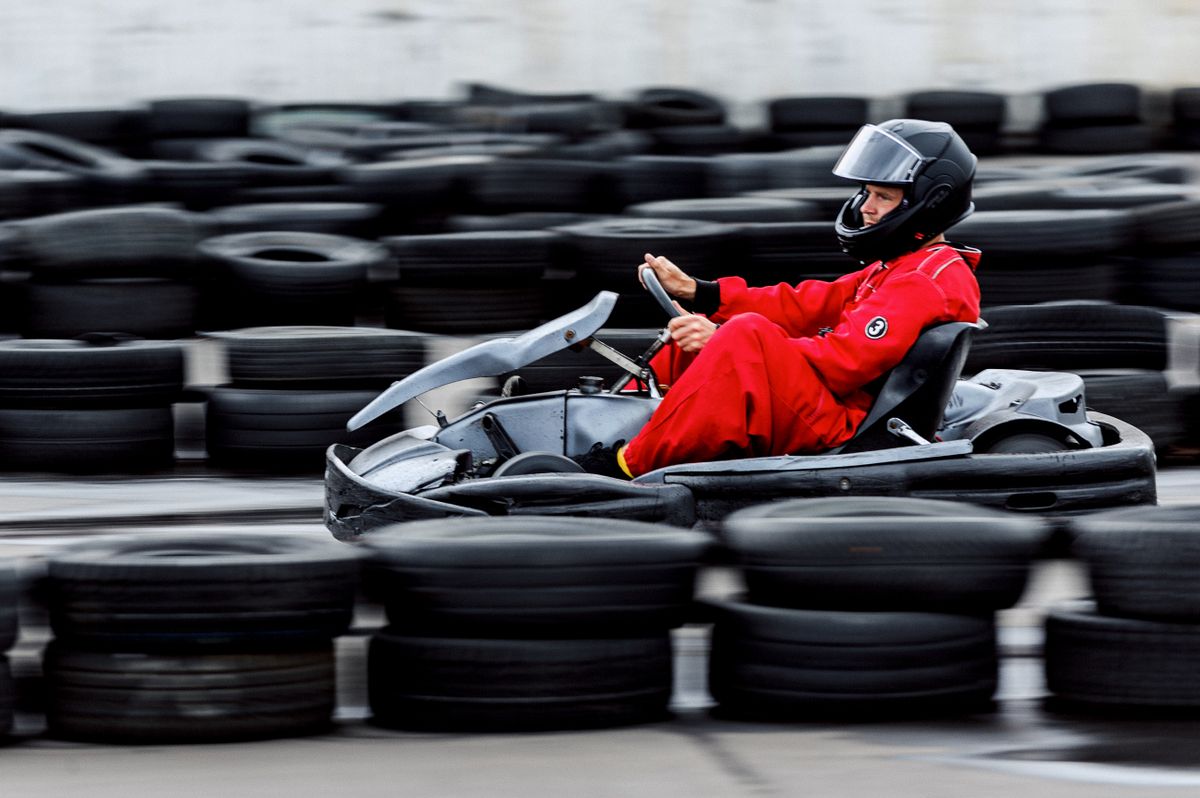 A driver in a red suit racing a go-kart past a tyre wall